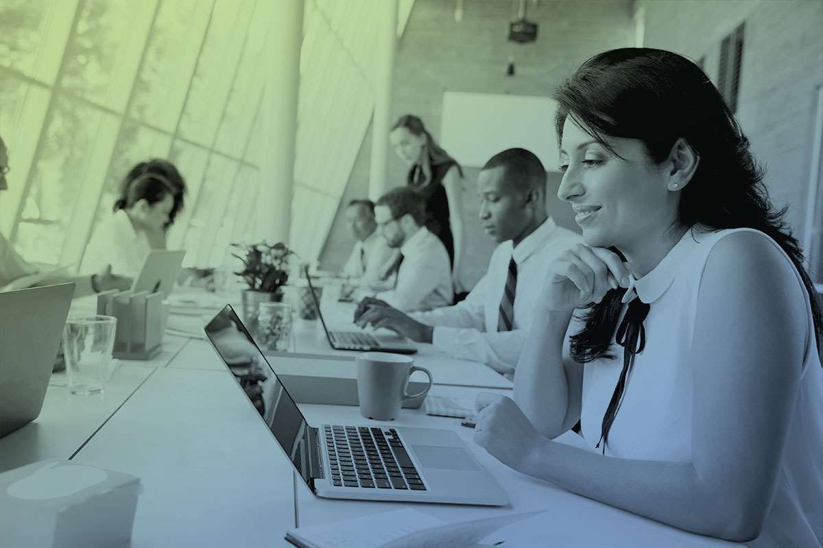 Woman at laptop computer in foreground with other workers in background