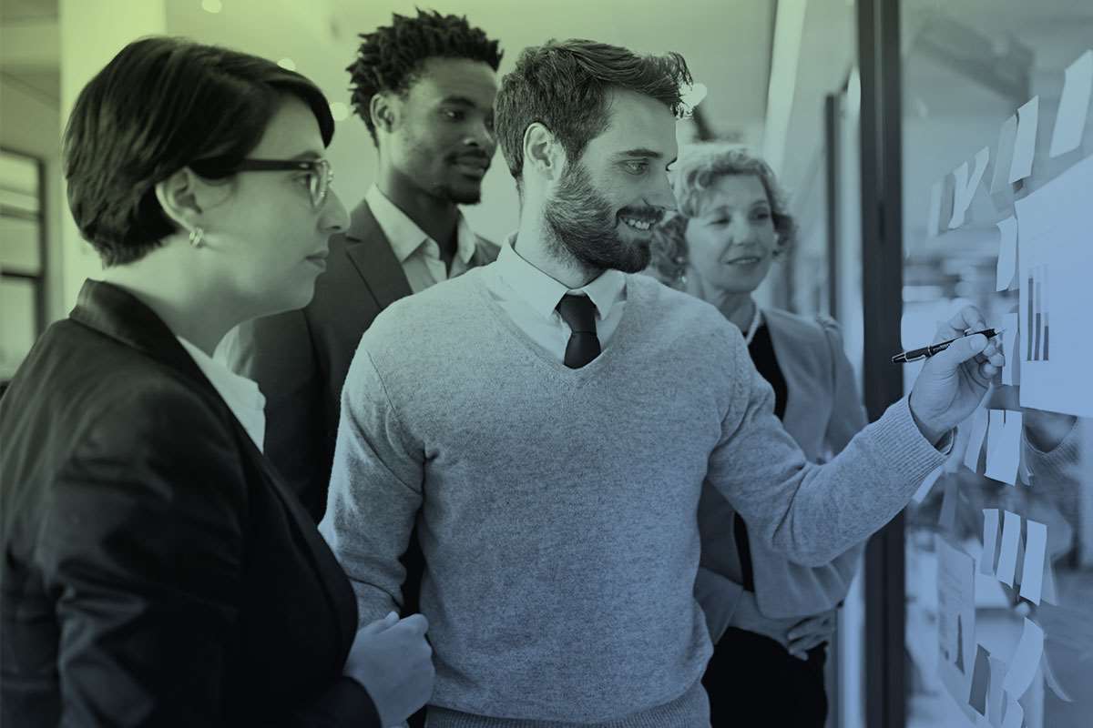 Man with group around him at whiteboard with sticky notes